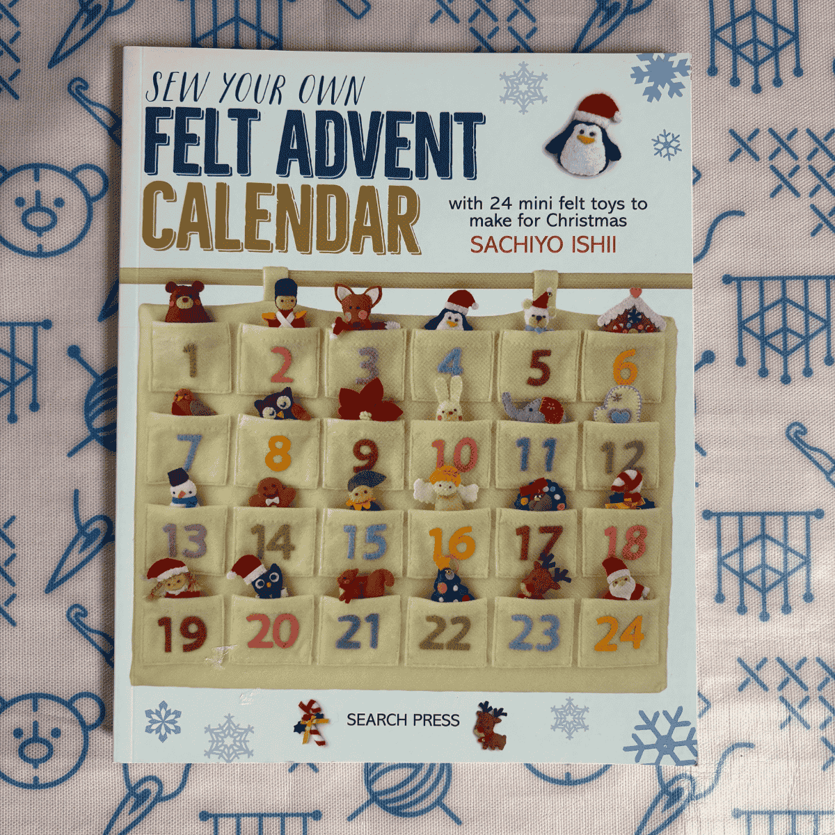 Book titled 'Sew Your Own Felt Advent Calendar' with felt toys on a patterned background