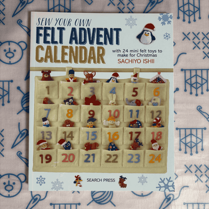 Book titled 'Sew Your Own Felt Advent Calendar' with felt toys on a patterned background